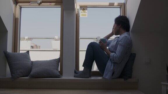 一个看似忧伤的女人坐在窗台上望着窗外沉思着