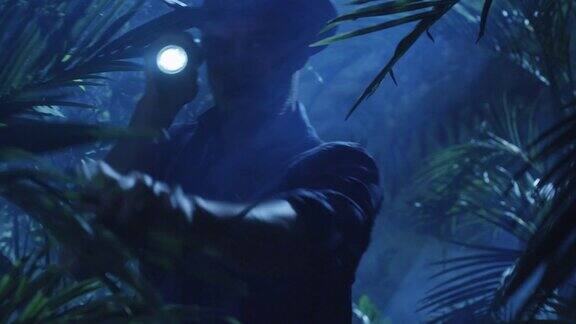 帽子冒险家在夜晚穿过丛林森林使用手电筒