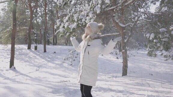 快乐的女孩微笑着在飘落的雪花中欣喜白色的雪花在阳光下闪闪发光从被雪覆盖的树上飘落的雪大自然美丽的冬天在冬天的森林里漫步慢动作