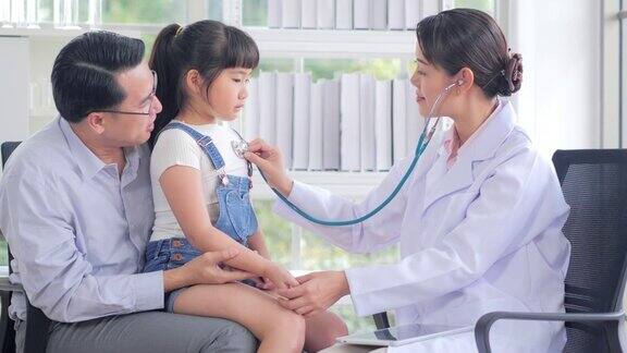 女儿科医生用听诊器检查可爱的小女孩孩子开心地笑着指着医生父亲抱着她的孩子中国和香港的医疗系统