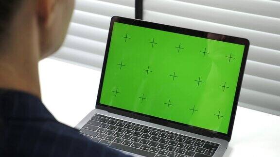 女商人在办公室桌上的笔记本电脑上使用绿色屏幕模型显示色度键
