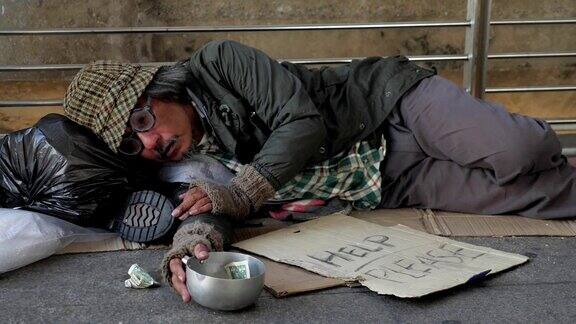 一个无家可归的老人穿着脏衣服躺在街上寻求帮助