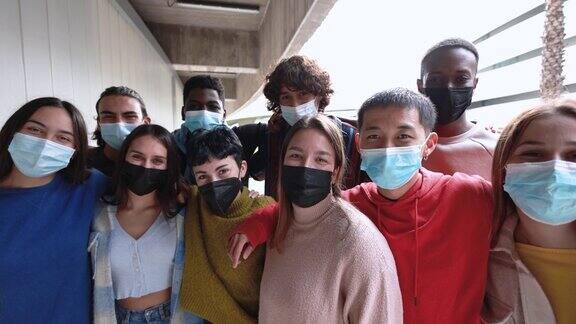 多种族的年轻朋友们戴着应对新冠肺炎疫情的安全口罩在户外的镜头前开心微笑