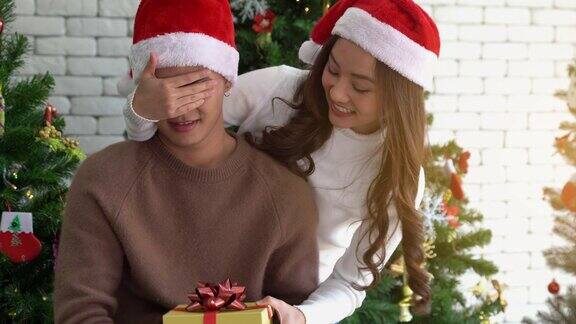 年轻的亚洲女孩惊喜她的男友庆祝圣诞节与礼盒