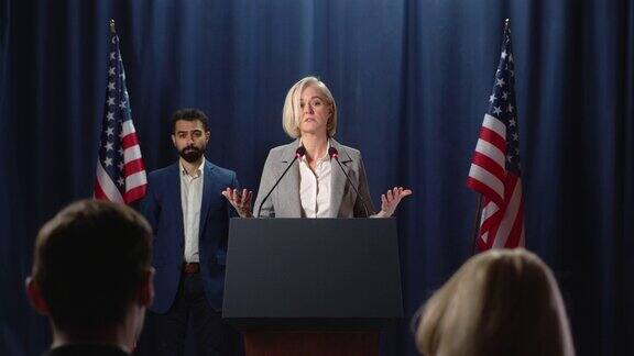 美国的争论一位矜持的女政治家站在绘有美国国旗的蓝色幕布前发表演讲