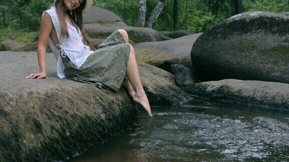 美丽的女孩坐在森林里的石头上在水里戏水
