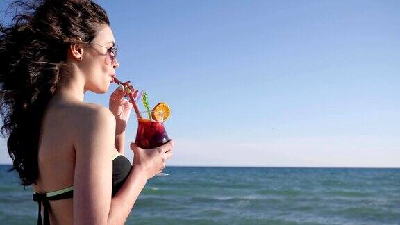 肖像微笑的女孩在海滩上性感的女人与卷发饮料多彩的鸡尾酒闪亮的海背景