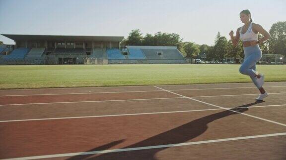美丽的健身女人在浅蓝色运动上衣和紧身裤是开始短跑在一个户外体育场她正在一个温暖的夏天跑步运动员在做运动练习跟踪拍摄