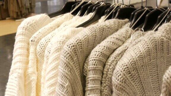 漂亮的女人编织的浅色毛衣挂在服装店的衣架上
