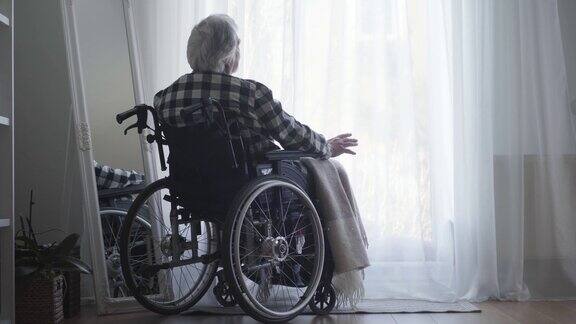 老白人男子坐在轮椅前的大窗户与窗帘关闭和思考孤独的老人独自在家度过一天老年退休残疾人