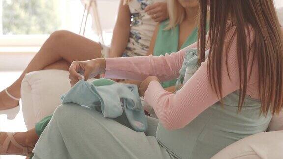 一名孕妇向朋友展示婴儿服装