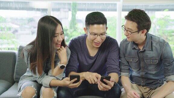 迷人的年轻亚洲朋友男女一起聊天在客厅的沙发上看手机