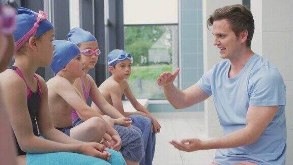 男教练在给坐在室内游泳池边上的孩子们讲解游泳课