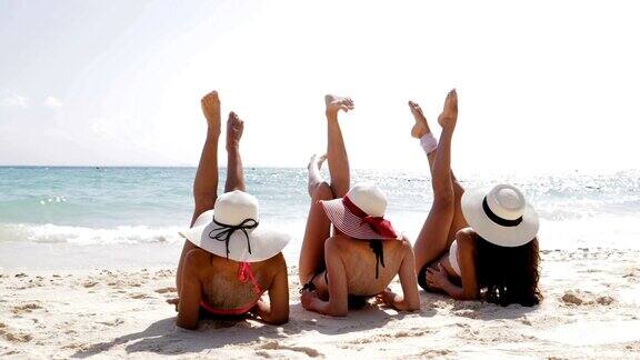 后视图三个女孩躺在沙滩上抬高腿享受日光浴女性游客在暑假