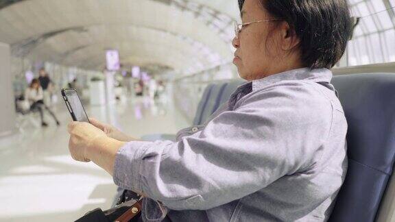 亚洲资深女乘客在候机楼用智能手机等待她的航班