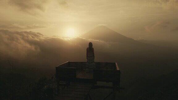 穿着长裙的女孩站在巴厘岛标志性的阿贡火山上日落