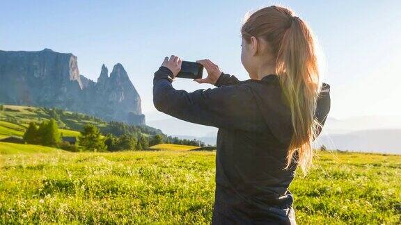 女人用智能手机拍摄盛开的草地背景是山脉