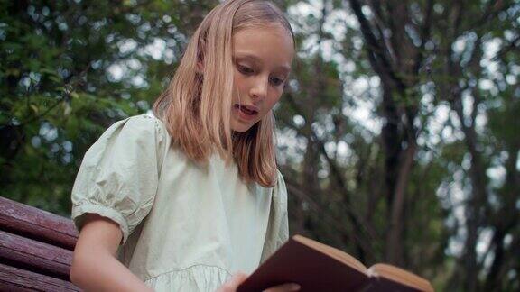 夏天一个十几岁的女孩坐在绿色花园的长椅上大声朗读年轻女子在夏日公园的户外看书