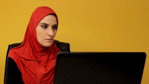 年轻的穆斯林女商人在办公室使用笔记本电脑