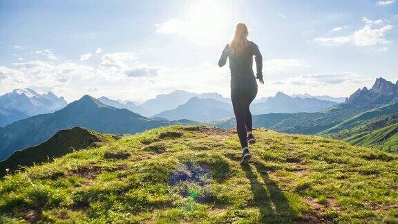 年轻的女运动员在山坡上向着太阳的草地上奔跑
