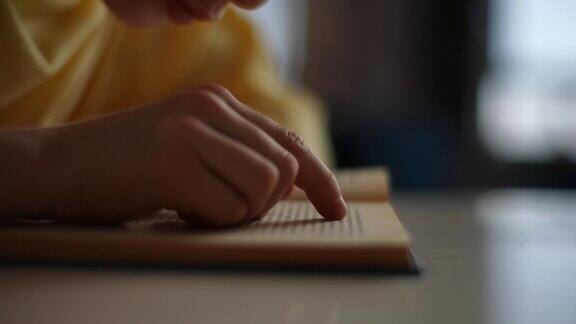 无法辨认的小学生男孩的特写快速阅读纸质书用手指沿着页坐在桌子上