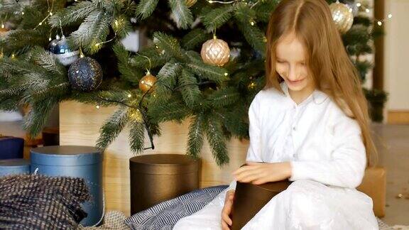 可爱的金发女孩正在打开暗金礼盒她收到坐在圣诞树旁快乐的童年和圣诞节庆祝概念