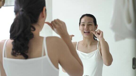 一个年轻的亚洲女人在家里的浴室里用牙线剔牙