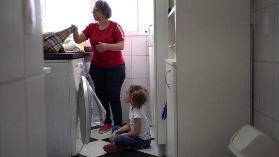 奶奶和孙女在洗衣房把脏衣服放进洗衣机里