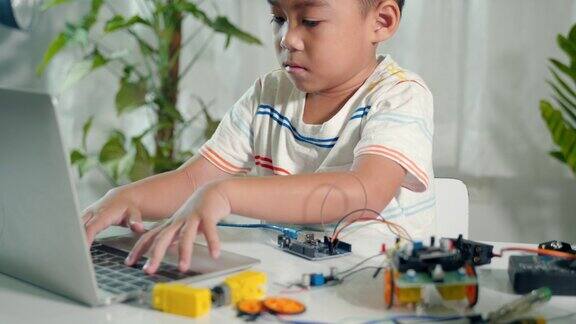 亚洲小男孩用笔记本电脑为Arduino机器人汽车学习编码和编程