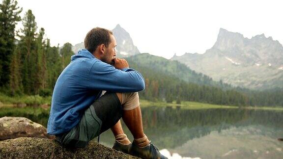 一个年轻人坐在山湖的岸边吹着口琴