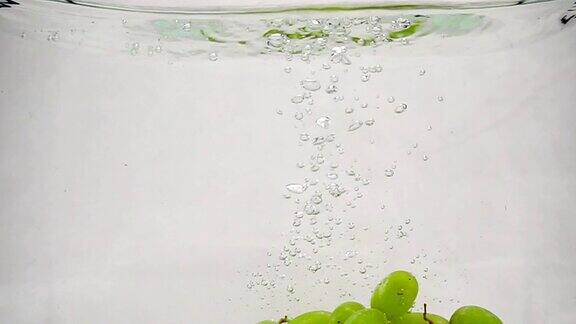 成熟的绿葡萄掉进带着气泡的纯净水中白色背景上的葡萄浆果的慢动作