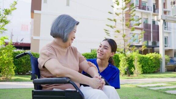 亚裔护理人员在户外照顾坐轮椅的残疾老妇人美丽的女孩医生帮助和照顾在公园养老院做物理治疗的老年残疾患者