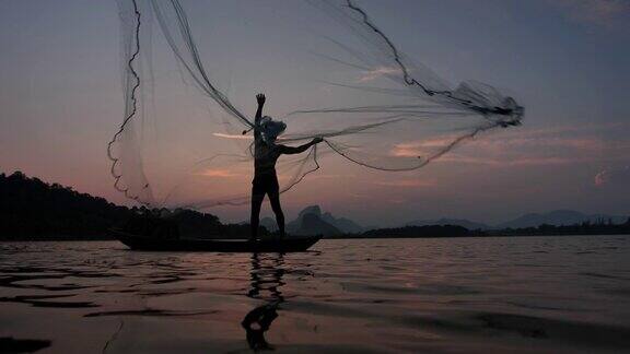 慢镜头剪影渔民抛出渔网在日落与船在湖渔民的生活方式泰国华富里以、亚洲