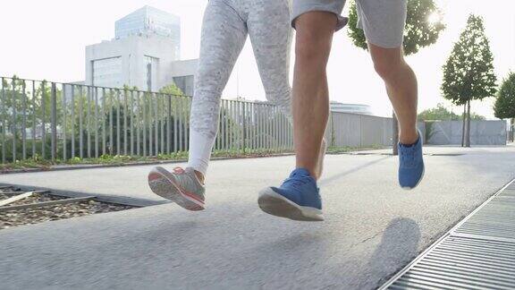 慢镜头特写:一对慢跑者在阳光明媚的日子里在城市街道上锻炼