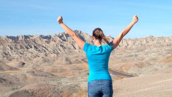 特写:在Badlands山顶快乐的女旅行者向天空举起手臂