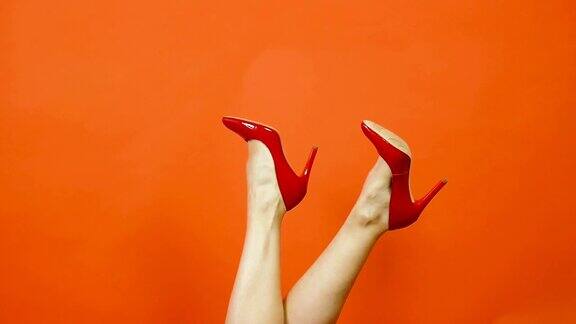 性感女人的腿在明亮的橙色背景红色高跟鞋它们从一边摇到另一边红专利鞋慢动作