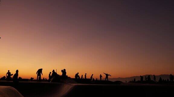 剪影的年轻跳高滑板骑长板夏季日落的背景威尼斯海洋海滩滑板公园加州洛杉矶青少年在滑板坡道极限公园组的青少年