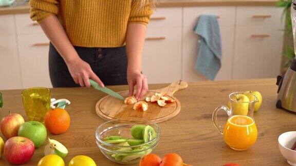 合上女士的手切一个橘子把它放在一个玻璃碗里准备一个健康的水果沙拉