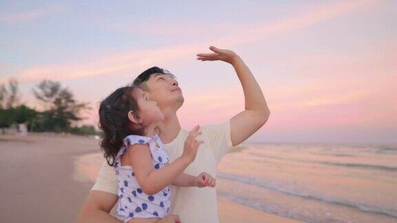 亚洲父亲抱着女儿在空中而散步在海滩上的黄昏时间度假