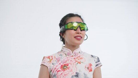 中国亚洲女性佩戴VR眼镜在春节期间与家人、亲戚和朋友在线见面和问候白色背景穿着旗袍白色花卉图案连衣裙
