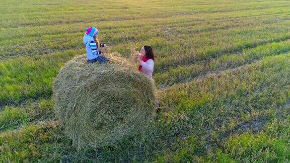小女孩坐在草堆上把稻草扔给妈妈