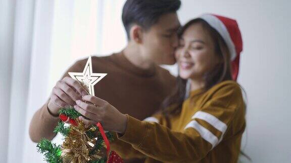 年轻的亚洲华人夫妇在装饰圣诞树时接吻庆祝圣诞节