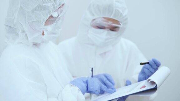 冠状病毒大流行期间两名身穿防护服的医护人员在写字板上讨论血液检测结果