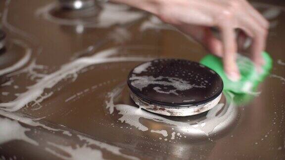 一个女人在厨房里用手清洗煤气炉她用带泡沫和清洁剂的绿色海绵擦拭