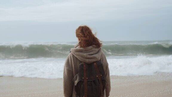 穿着灰色羊毛衫的女孩在阴天寒冷的天气里独自走在空旷的海边