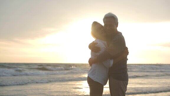 落日余晖中一对亚洲老年夫妇在海滩上拥抱对方