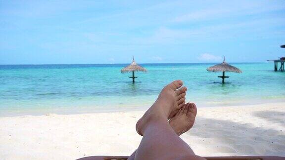 游客光着脚坐在金色沙滩长椅上指出热带海洋天堂