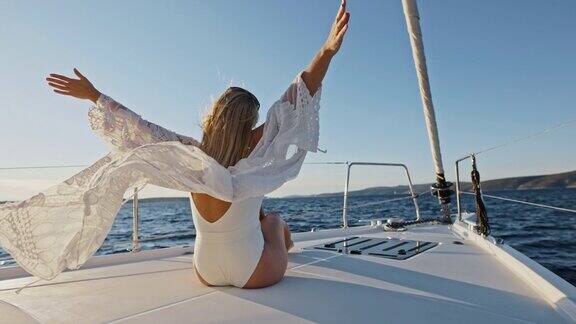 一名年轻女子在帆船甲板上享受微风时双手高举在空中