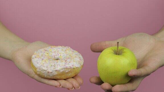 手里拿着甜甜圈和苹果选择甜甜圈而不是苹果健康或垃圾食品