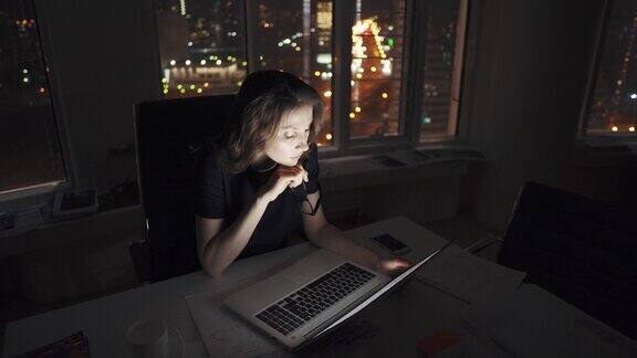 经理在办公室工作到很晚年轻的女企业家在夜深的城市灯光下在笔记本电脑上工作
